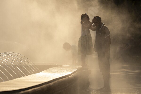 A little girl touches her father's head as they are engulfed by mist from a public fountain in Bucharest, Romania, Thursday, July 13, 2023. (AP Photo/Andreea Alexandru)