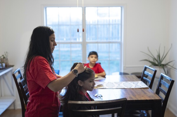 Liz Hurtado adjusts her daughter Lina Lazo's hair before she walks to the school bus on Tuesday, Feb. 6, 2024, in Virginia Beach, VA.  Hurtado has spent years advocating for electric buses.  (AP Photo/Tom Brenner)