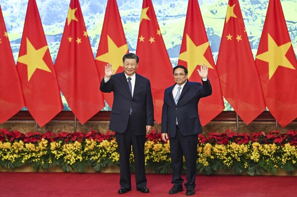 Vietnam's Prime Minister Pham Minh Chinh, right, and the China's President Xi Jinping wave to media members as they pose for a photo during a meeting at the government office in Hanoi, Vietnam, Wednesday, Dec. 13, 2023. (Nhac Nguyen/Pool Photo via AP)