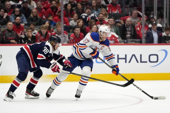 Washington Capitals defenseman Rasmus Sandin (38) tries to knock the puck away from Edmonton Oilers center Connor McDavid (97) in the second period of an NHL hockey game, Friday, Nov. 24, 2023, in Washington. (AP Photo/Mark Schiefelbein)