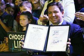 FILE - Florida Gov. Ron DeSantis holds up a 15-week abortion ban law after signing it on April 14, 2022, in Kissimmee, Fla. Reproductive health providers sued Florida on Wednesday, June 1, 2022, alleging that the law violates a provision in the state constitution guaranteeing a person’s right to privacy, “including the right to abortion.” (AP Photo/John Raoux, File)
