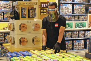 FILE - In this Monday, June 15, 2020 file photo, an employee wearing protective gear arrange boxes of Lego at a toy store at the Senayan City, in Jakarta, Indonesia. Sales of Lego sets surged in 2020 as more children stayed home during global pandemic lockdowns - and parents bought the colorful plastic brick toys to keep them entertained during weeks of isolation. The privately-held Danish company said its net profit rose 19% to 9.9 billion kroner ($1.6 billion) as sales jumped 21% and it grew its presence in its 12 largest markets. (AP Photo/Tatan Syuflana, file)