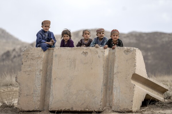 GALLERY - Children sit on a toppled cement barrier on the side of a road to watch passing cars in a village in a remote region of Afghanistan, on Sunday, Feb. 26, 2023. (AP Photo/Ebrahim Noroozi)