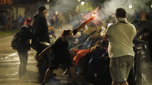 FILE - A protester tosses an object toward police during clashes outside the Kenosha County Courthouse, Aug. 25, 2020, in Kenosha, Wis., on a third night of unrest following the shooting of a Black man, Jacob Blake, whose attorney said he was paralyzed after being shot multiple times by police. On Tuesday, July 4, 2023, two freelance photographers filed a lawsuit alleging that police unlawfully shot them with rubber bullets during a protest over police racism in Wisconsin three years ago. (AP Photo/David Goldman, File)