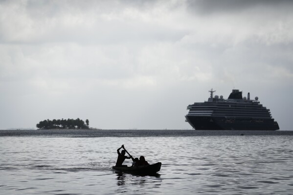 A man paddles near Gardi Sugdub Island where a cruise ship floats amid the San Blas archipelago off Panama's Caribbean coast, Sunday, May 26, 2024. Due to rising sea levels, about 300 Guna Indigenous families will relocate to new homes, built by the government, on the mainland. (AP Photo/Matias Delacroix)