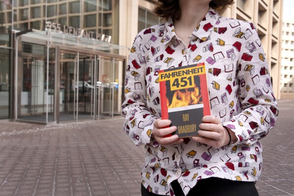 A person wearing a shirt covered in books holds a copy of the novel "Fahrenheit 451" while protesting in support of the Institute of Museum and Library Services (IMLS), Thursday, March 20, 2025, outside the IMLS in Washington, after hearing that DOGE had shown up to the office. (AP Photo/Jacquelyn Martin)