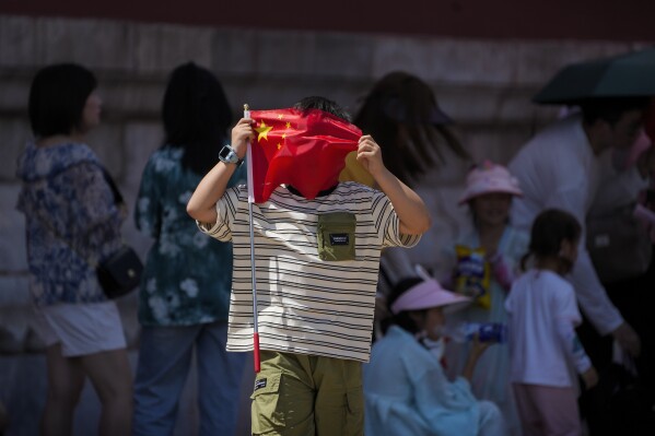 A boy uses a national flag to shield himself from the sun as visitors line up to enter the Forbidden City on a sweltering day in Beijing, Friday, July 7, 2023. (AP Photo/Andy Wong)