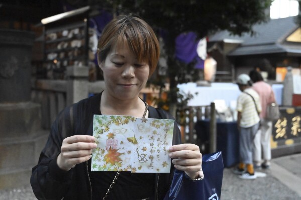 Masami Takeda, a visitor to Onoterusaki Jinja, shows off Goshuin, a seal stamp certifying her visit that comes with elegant calligraphy and the season’s drawings, in Tokyo, on Sept. 18, 2023. Takeda brought her 6-year-old grandson, and they picked up a stamp with autumn leaves. "I never think I visit religious sites," Takeda says. "But I now pray for my grandson’s health." (AP Photo/Ayaka McGill)