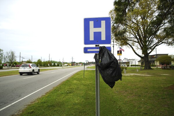 A garbage bag hangs from a hospital sign along U.S. 17 in Williamston, N.C., on Thursday, April 11, 2024. After the closing of Martin General, Williamston's only hospital, residents there say they're not only worried about their health but they've lost trust in politicians. The struggle to reopen its only emergency room could signal trouble for President Joe Biden's re-election campaign, which is centered around his health care accomplishments. (AP Photo/Allen G. Breed)