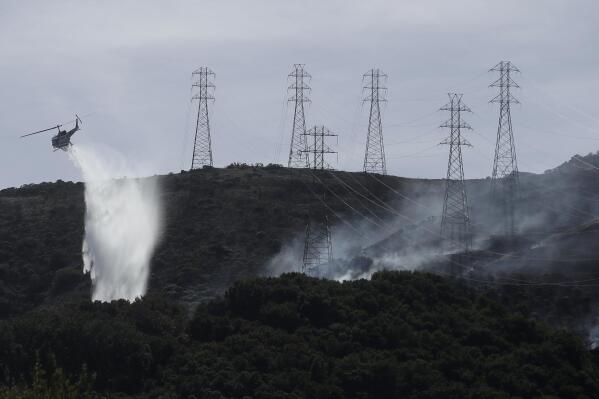 FILE - In this Oct. 10, 2019, file photo, a helicopter drops water near power lines and electrical towers while working at a fire on San Bruno Mountain near Brisbane, Calif. California energy leaders on Friday, May 6, 2022 said the state may see an energy shortfall this summer. Threats from drought, extreme heat and wildfires, are among the issues that will create challenges for energy reliability this summer and in the coming years. (AP Photo/Jeff Chiu, File)