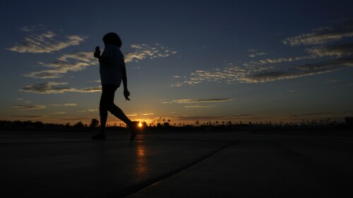 Janice Edwards listens to a podcast on her phone as she walks at sunrise Tuesday, July 11, 2023, in Yuma, Ariz. Edwards takes her walks starting before dawn to avoid the heat. Even desert residents accustomed to scorching summers are feeling the grip of an extreme heat wave smacking the Southwest this week. Arizona, Nevada, New Mexico and Southern California are getting hit with 100-degree-plus temps and excessive heat warnings. (AP Photo/Gregory Bull)