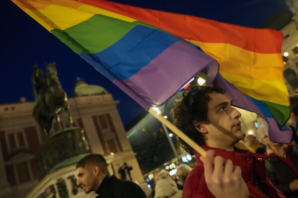 A man waves a rainbow flag in front of the monument of late Serbian Duke Mihailo Obrenovic during a protest, in downtown Belgrade, Serbia, Wednesday, March 6, 2024. Rights activists and members of LGBTQ+ community in Serbia on Wednesday held a protest following a reported case of police harassment of a young gay men and a bisexual woman. (AP Photo/Darko Vojinovic)