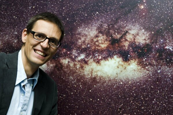 FILE - In this Wednesday, Sept. 16, 2009 file photo Swiss astrophysicist Didier Queloz poses in front of the picture of the Milky Way at the Geneva Observatory in Geneva, Switzerland. The 2019 Nobel prize in Physics was given to James Peebles "for theoretical discoveries in physical cosmology," and the other half jointly to Michel Mayor and Didier Queloz "for the discovery of an exoplanet orbiting a solar-type star," said Prof. Goran Hansson, secretary-general of the Royal Swedish Academy of Sciences that chooses the laureates.  (Salvatore Di Nolfi, Keystone via AP)