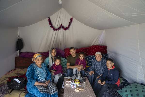 Ahmed Aazab, center, sits with his wife Khadija Bouzegit, parents Hocine and Zahra, and children in their tent, after they were displaced by the September earthquake, in Moulay Brahim, outside Marrakech, Morocco, Saturday, Oct. 7, 2023. Morocco has pledged to rebuild from a September earthquake in line with its architectural heritage. Villagers and architects agree that earthquake-safe construction is a top priority. That’s created a push for modern building materials. But the government says it wants to rebuild in line with Morocco’s cultural and architectural heritage. (AP Photo/Mosa'ab Elshamy)