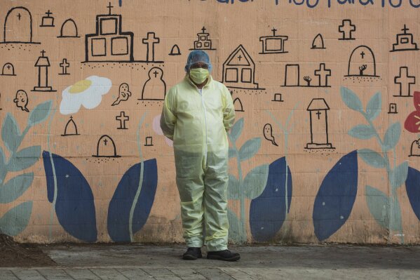 Funeral home worker Manuel Castro, wearing a full protective gear to protect himself from the spread of the new coronavirus, waits to enter La Verbena cemetery in Guatemala City, Wednesday, July 29, 2020. (AP Photo/Moises Castillo)
