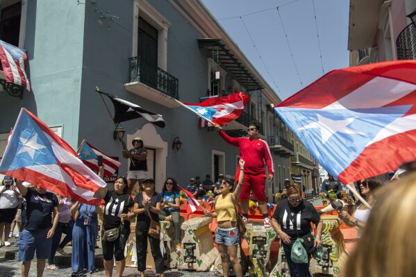 Demonstrators, some waving Puerto Rican national flags, gather in front of the governor's mansion La Fortaleza, in San Juan, Puerto Rico, Wednesday, July 24, 2019. Hundreds of thousands of Puerto Rico have been outraged by leaked, obscenity-laced online chats between Gov. Ricardo Rossello and his advisers, and have protested for nearly two weeks demanding his resignation. (AP Photo/Dennis M. Rivera Pichardo)