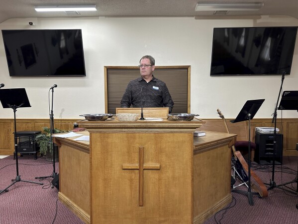 Pastor Kenny Batson stands at the pulpit of Grace Fellowship Church on Nov. 16, 2023, in El Dorado Springs, Mo. Batson was convicted of a series of crimes in the 1990s but became a Christian pastor after being released from prison. He was pardoned by Missouri Gov. Mike Parson. (AP Photo/David A.Lieb)