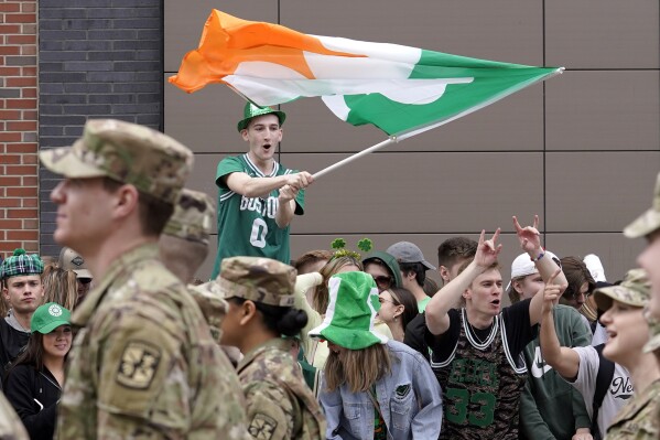 FILE - A spectator, top, waves a flag that features a likeness of a shamrock as members of the Boston University ROTC program, left, march past during the St. Patrick's Day parade, Sunday, March 20, 2022, in Boston's South Boston neighborhood. (AP Photo/Steven Senne, File)