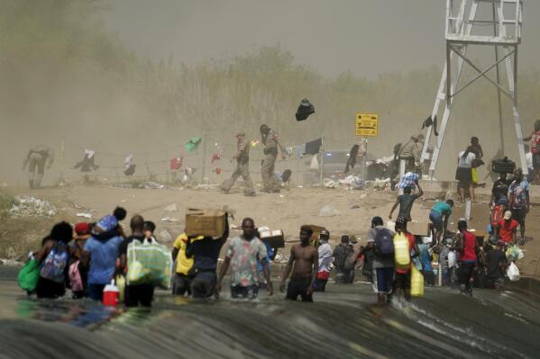 A dust storm moves across the area as Haitian migrants use a dam to cross into and from the United States from Mexico, Saturday, Sept. 18, 2021, in Del Rio, Texas. The U.S. plans to speed up its efforts to expel Haitian migrants on flights to their Caribbean homeland, officials said Saturday as agents poured into a Texas border city where thousands of Haitians have gathered after suddenly crossing into the U.S. from Mexico. (AP Photo/Eric Gay)