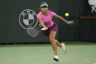 FILE - Emma Raducanu, of Britain, returns a shot to Iga Swiatek, of Poland, at the BNP Paribas Open tennis tournament Tuesday, March 14, 2023, in Indian Wells, Calif. Raducanu will miss the French Open and Wimbledon after announcing that minor surgery on both hands and an ankle will sideline her for “the next few months.” The 2021 U.S. Open champion has struggled with injuries in recent months and pulled out of the Madrid Open because of a hand problem. (AP Photo/Mark J. Terrill, File)