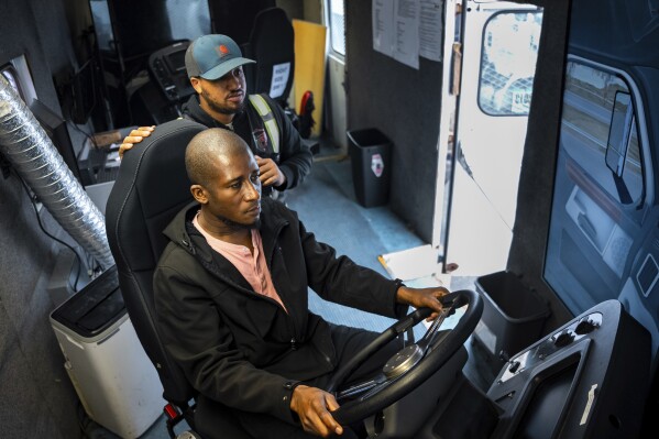 Trucking student Mohammed Kamal, left, overseen by instructor Tom Panton, practices driving a tractor-trailer truck in a simulation at the Driving Academy on Tuesday, June 10, 2025 in Linden, N.J. (AP Photo/Angelina Katsanis)