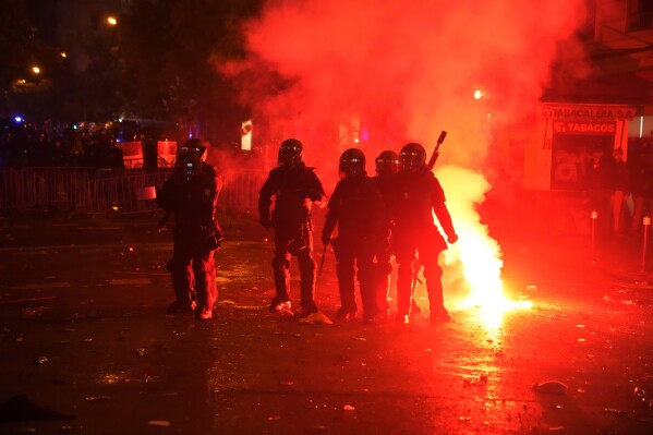 Riot police officers take position in a cloud of tear gas and flares during a protest by right wing demonstrators near the national headquarters of Spain's Socialist Party in Madrid, Spain, Tuesday, Nov. 7, 2023. The Spanish capital saw its second night in a row of clashes between police and protesters who oppose negotiations between Spain's acting government and Catalan separatist parties over a possible amnesty for thousands involved in Catalonia's independence movement. (AP Photo/Paul White)