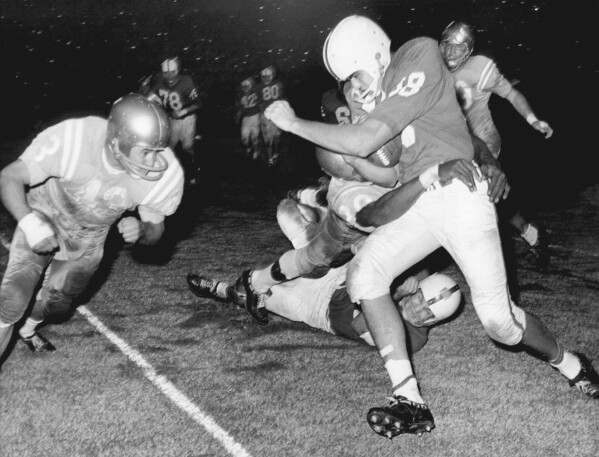 North Carolina State quarterback Roman Gabriel is in the clutches of a UCLA player as another is driving in at left as he was stopped after an end sweep during an NCAA college football game Oct. 29, 1960, in Los Angeles. Gabriel, the former North Carolina State quarterback who was the 1969 NFL MVP with the Los Angeles Rams, died Saturday, April 20, 2024. He was 83. (AP Photo/Harold P. Matosian)