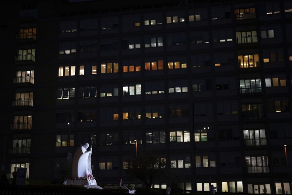 A statue of late Pope John Paul II is lit outside the Agostino Gemelli Polyclinic in Rome, Thursday, March 13, 2025, where Pope Francis is being treated for bilateral pneumonia since Feb. 14. (AP Photo/Domenico Stinellis)