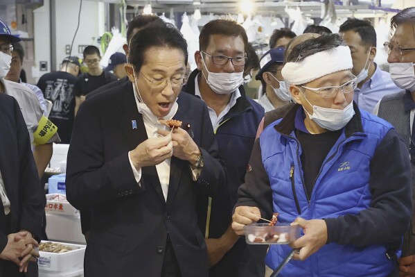 Japan's Prime Minister Fumio Kishida, front left, tries a seafood at Toyosu fish market in Tokyo Thursday, Aug. 31, 2023. Kishida visited the fish market to highlight fish safety and assess the impact of China's ban on Japanese seafood. (Kyodo News via AP)