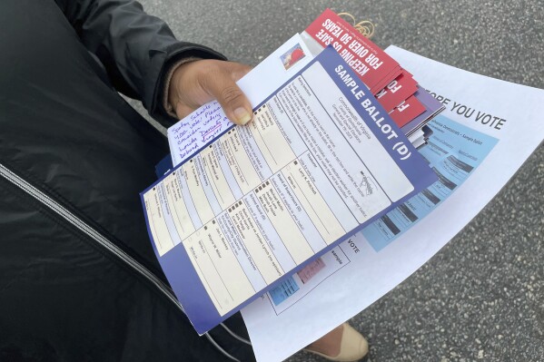 A poll volunteer displays a misleading sample ballot that a candidate for Spotsylvania County clerk of court was handing out at an early voting location in Fredericksburg, Va., Oct. 17, 2023. The blue sheet marked "(D)" appears to come from the local Democratic Party but was distributed at the scene by Nick Ignacio, the independent candidate for court clerk, with his name checked. Ignacio also gave out red sample ballots that resemble the Republican one, implying to voters who didn't look too closely that both parties have endorsed his bid in Tuesday's elections. Neither has. A judge subsequently barred Ignacio from distributing the sheets. (AP Photo/Cal Woodward)