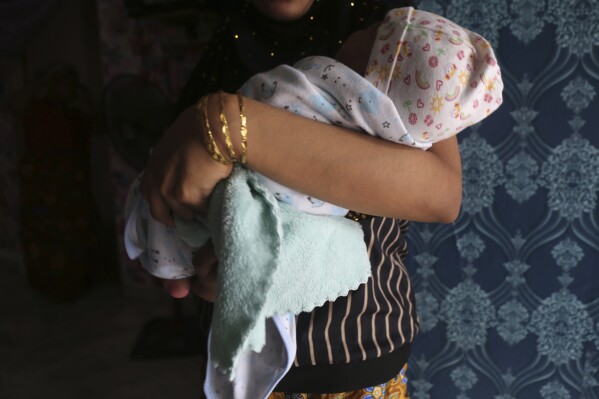 Rohingya child bride, R, age 16, holds her newborn baby while standing in an apartment in Kuala Lumpur, Malaysia, on Oct. 4, 2023. R left Bangladesh's refugee camps for Malaysia in 2022 to marry her 27-year-old husband as conditions in the camps deteriorated. R says she wasn't ready to have a baby, but felt lonely and is now glad to have the company. (AP Photo/Victoria Milko)