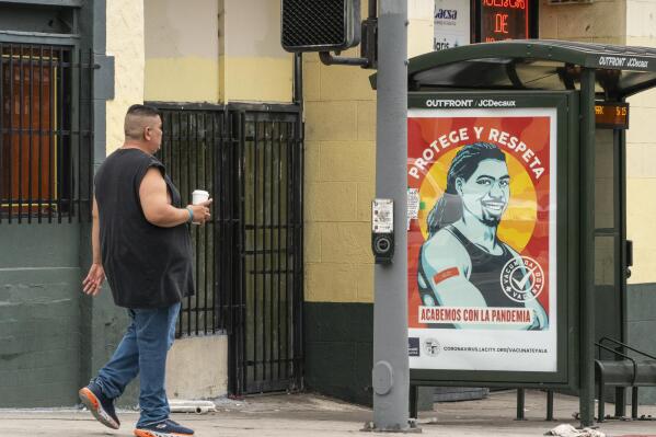 A pedestrian walks past a banner promoting vaccinations at the Pico-Union district in Los Angeles, Monday, July 26, 2021. The City of Los Angeles advertisement reads in Spanish: "Protect and Respect, Let's End the Pandemic." Pico-Union is the fourth most dense neighborhood in Los Angeles, home to a large immigrant community. The state of California said it would require proof of vaccination or weekly testing for all state workers and millions of public- and private-sector health care employees starting in August. (AP Photo/Damian Dovarganes)