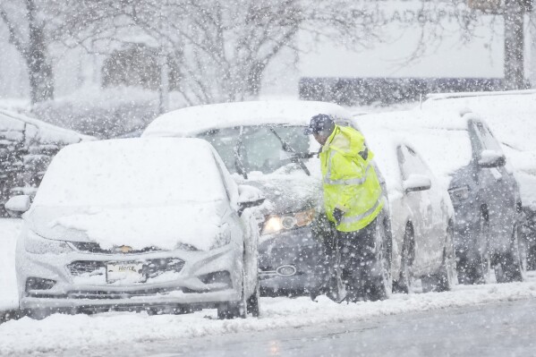 A person cleans off a car during a winter snow storm in Philadelphia, Tuesday, Feb. 13, 2024. (AP Photo/Matt Rourke)