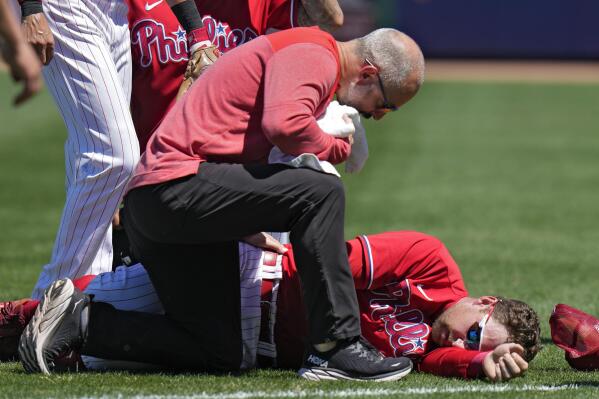 A trainer checks on Philadelphia Phillies first baseman Rhys Hoskins after he was injured fielding a ground ball by Detroit Tigers' Austin Meadows during the second inning of a spring training baseball game Thursday, March 23, 2023, in Clearwater, Fla. Hoskins had to be carted off the field. (AP Photo/Chris O'Meara)