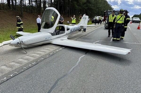 In this image provided by the Moncure, N.C., Fire Department, emergency personnel and law enforcement look over the scene after a small plane, experiencing engine problems, made an emergency landing along Route 1, Thursday afternoon, April 4, 2024, in Moncure, N.C., near Raleigh Executive Jetport at Sanford-Lee County Airport. The plane struck two vehicles as it landed, but no injuries were reported, authorities said. (Moncure Fire Department via AP)