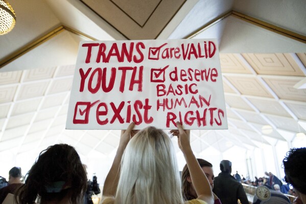 FILE - Hunter Schafer, of Raleigh, holds a sign supporting transgender youth during a special session of the North Carolina General Assembly in Raleigh, N.C., Dec. 21, 2016. While Republican lawmakers in North Carolina gear up to override vetoes of bills restricting rights of transgender people, courts across the country have been taking opposing stances on similar laws. If the override efforts are successful, the state will join most other GOP-controlled ones in limiting gender-affirming care such as puberty blockers and hormone treatments for minors. (AP Photo/Ben McKeown, File)