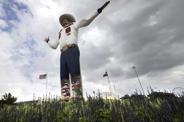 FILE - Bluebonnets, the state flower of Texas, surround Big Tex as storm clouds move in above, Friday, Sept. 27, 2013, in Dallas. (AP Photo/Tony Gutierrez, File)