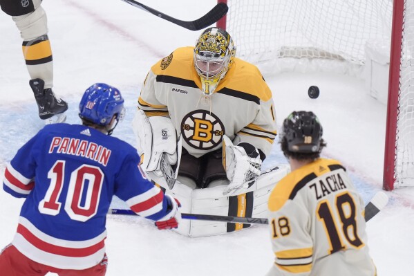 New York Rangers left wing Artemi Panarin (10) hits the puck past Boston Bruins goaltender Jeremy Swayman (1) to score in the second period of an NHL hockey game as Bruins center Pavel Zacha (18) looks on, Thursday, March 21, 2024, in Boston. (AP Photo/Steven Senne)