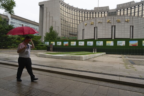 A man with an umbrella passes by China's central bank also known as People's Bank of China, in Beijing, Thursday, July 25, 2024. (AP Photo/Ng Han Guan, File)