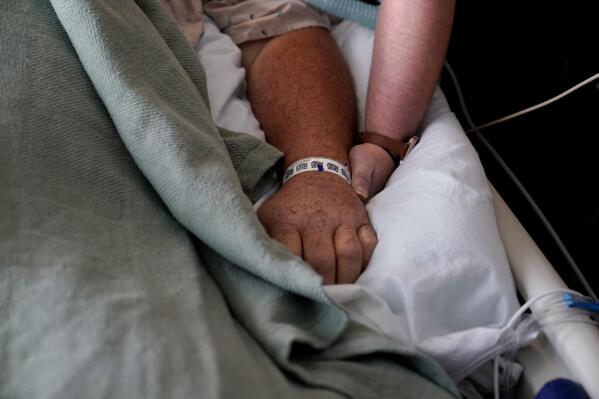 FILE - A woman, who is on oxygen as she recovers from COVID-19, holds the hand of her husband, who also contracted COVID-19, as he is kept alive with the help of an oxygenation machine at a medical center in Shreveport, La., Aug. 18, 2021. A majority of adults in the U.S. say health care is not handled well in the country. That's according to a new poll from The Associated Press-NORC Center for Public Affairs Research. (AP Photo/Gerald Herbert, File)