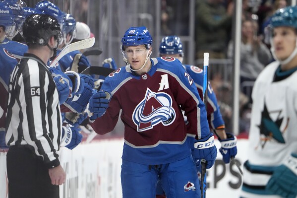 Colorado Avalanche center Nathan MacKinnon, center, is congratulated after scoring as he passes by the team box in the second period of an NHL hockey game against the San Jose Sharks, Sunday, Dec. 17, 2023, in Denver. (AP Photo/David Zalubowski)