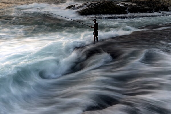 A fisherman casts his fishing line into the Mediterranean Sea from a rocky area along the Beirut coastline, on a sweltering hot day, in Beirut, Lebanon, Saturday, July 27, 2024. (AP Photo/Hassan Ammar)