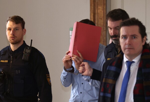 A 31-year-old American man accused of murder is led into the courtroom at the regional court in Kempten, Southern Germany, Monday Feb. 19, 2024. An American man on Monday admitted to charges of murder and rape after he allegedly pushed two U.S. women down a ravine, fatally injuring one of them near Germany's Neuschwanstein castle last year. (Karl-Josef Hildenbrand/dpa via AP)