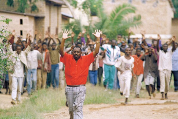 FILE - Rwandan refugees hold their hands up and ask for help from Belgian soldiers, who had come to a psychiatric hospital compound outside of Kigali on April 13, 1994. People are patients of this hospital. (AP Photo/Karsten Thielker, File)