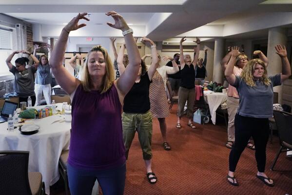 CORRECTS INSTRUCTORS NAME TO EMILY DANIELS FROM EMILY RILEY Instructor Emily Daniels, left, raises her arms while leading a workshop helping teachers find a balance in their curriculum while coping with stress and burnout in the classroom, Tuesday, Aug. 2, 2022, in Concord, N.H. School districts around the country are starting to invest in programs aimed at address the mental health of teachers. Faced with a shortage of educators and widespread discontentment with the job, districts are hiring more therapist, holding trainings on self-care and setting up system to better respond to a teacher encountering anxiety and stress. (AP Photo/Charles Krupa)