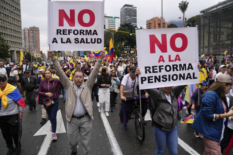 Anti-government demonstrators holding signs reading in Spanish "No to the Health Reform", left, and "No to the Pension Reform" march to protest economic and social reforms pushed by the government of President Gustavo Petro and his proposal to convene a constituent assembly in Bogota, Colombia, Sunday, April 21, 2024. (AP Photo/Fernando Vergara)