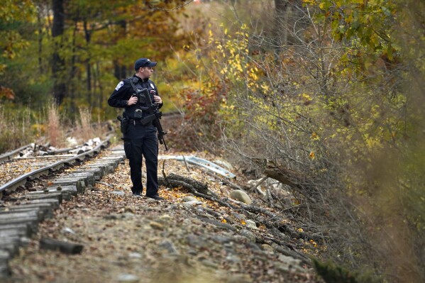 A police officer searches along railroad tracks near the Androscoggin River for the suspect in this week's deadly mass shootings, Friday, Oct. 27, 2023, in Lisbon, Maine. The manhunt continues for the man who killed at least 18 in separate shootings at a bowling alley and restaurant in Lewiston on Wednesday. (AP Photo/Robert F. Bukaty)