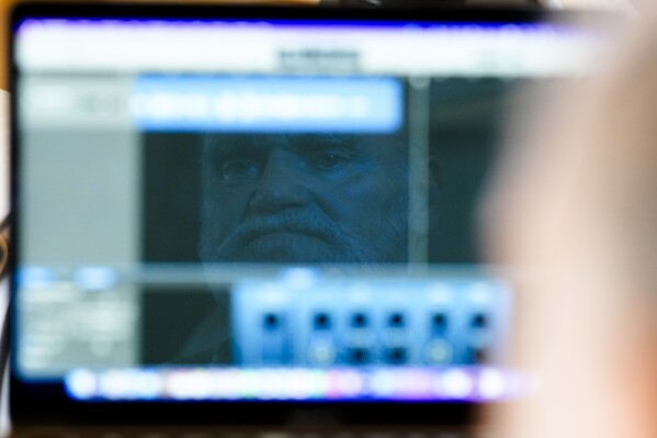 Michael Bommer, who is terminally ill with colon cancer, is reflected in his computer screen during a meeting with The Associated Press at his home in Berlin, Germany, Wednesday, May 22, 2024. Bommer, who has only a few more weeks to live, teamed up with friend who runs the AI-powered legacy platform Eternos to 