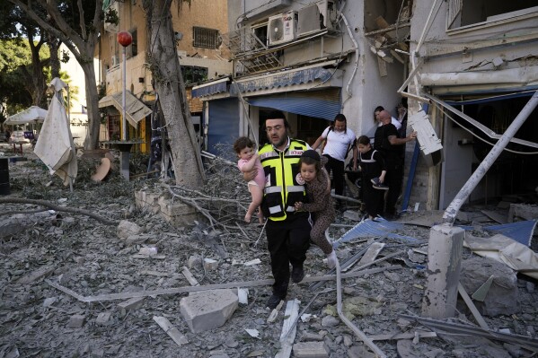 A rescue worker carries two children as residents evacuate from the site where a missile launched from Iran struck Haifa, Israel, Sunday, June 22, 2025. (AP Photo/Baz Ratner)