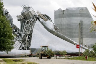 Iowa Department of Transportation workers help with tree debris removal as grain bins from the Archer Daniels Midland facility are seen severely damaged in Keystone, Iowa, on Wednesday, Aug. 12, 2020. Damage estimates from a rare wind storm that slammed Iowa and some other parts of the Midwest in August are growing, with the total now at $7.5 billion, according to a new report. (Jim Slosiarek/The Gazette via AP)
